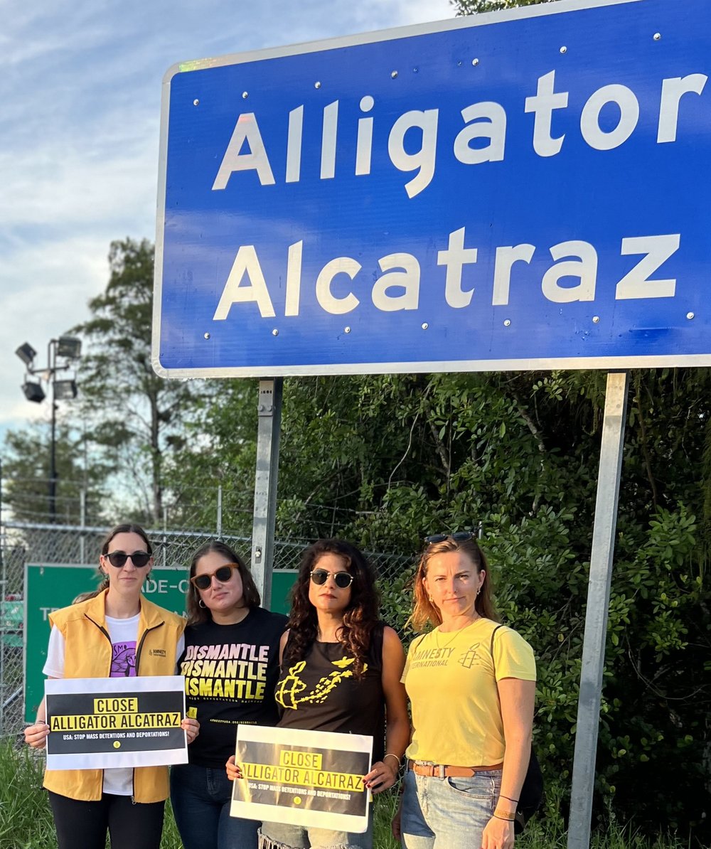 Amnesty Aktivist*innen vor dem Ortschild «Alligator Alcatraz»