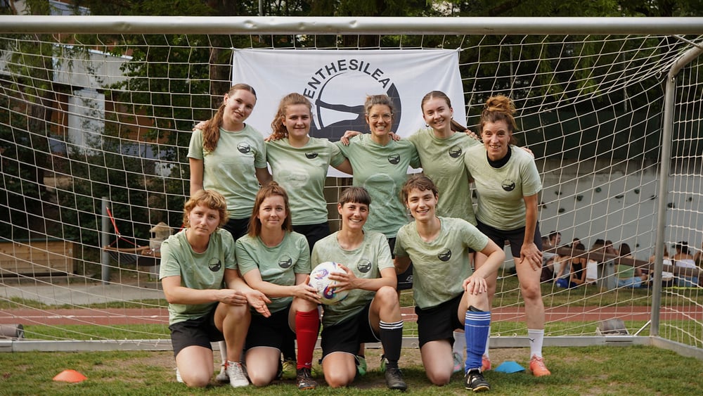 Die Spielerinnen posieren mit dem Ball in der Hand in ihren salbeigrünen Trikots.