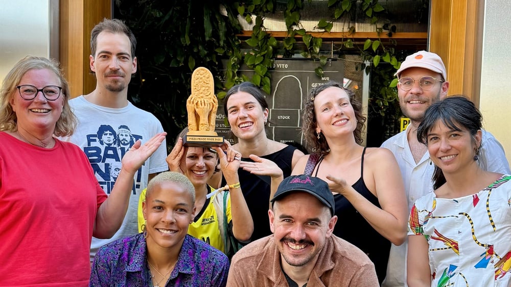 Teilnehmende des Events mit dem Pizza-Peace-Prize, der von Lisa Salza hochgehoben wird.