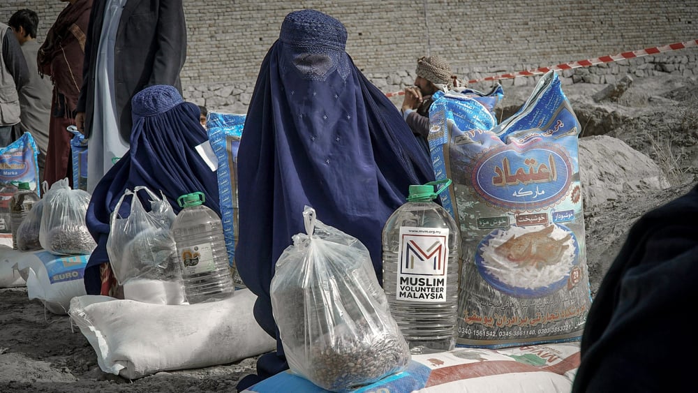 Zwei vollverschleierte Frauen sitzen auf dem Boden mit Wasserkanistern, die sie vermutlich verkaufen.