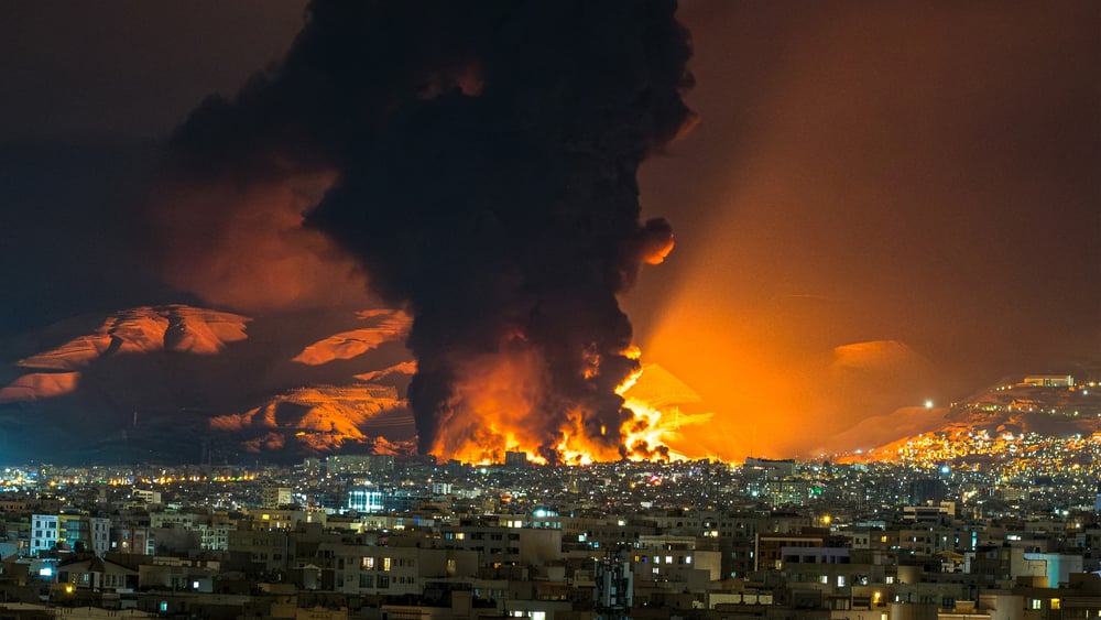 Ein Blick über die nächtliche Stadt, aus welcher Flammen und Rauch hochschiessen.