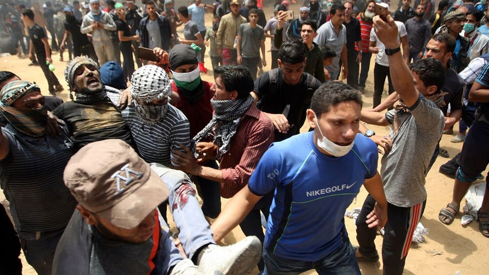 Palästinenser tragen im Gazastreifen einen verletzten Demonstranten weg. 14. Mai 2018. © Keystone/Newscom/Ismael Mohamad