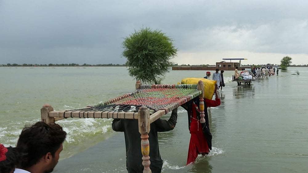 Menschen verlassen ihre Dörfer und tragen ihre Habseligkeiten durch überschwemmte Ebenen, um in höher gelegene Gebiete im südlichen Punjab zu erreichen, 25. August 2022. © Getty / Shahid Saeed Mirza