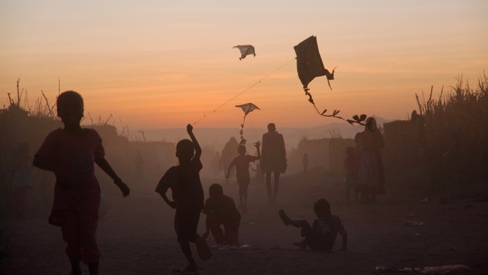Die Silouetten von Kindern, die Drachen fliegen lassen, im Dunst im Sonnenauf- oder Untergang.