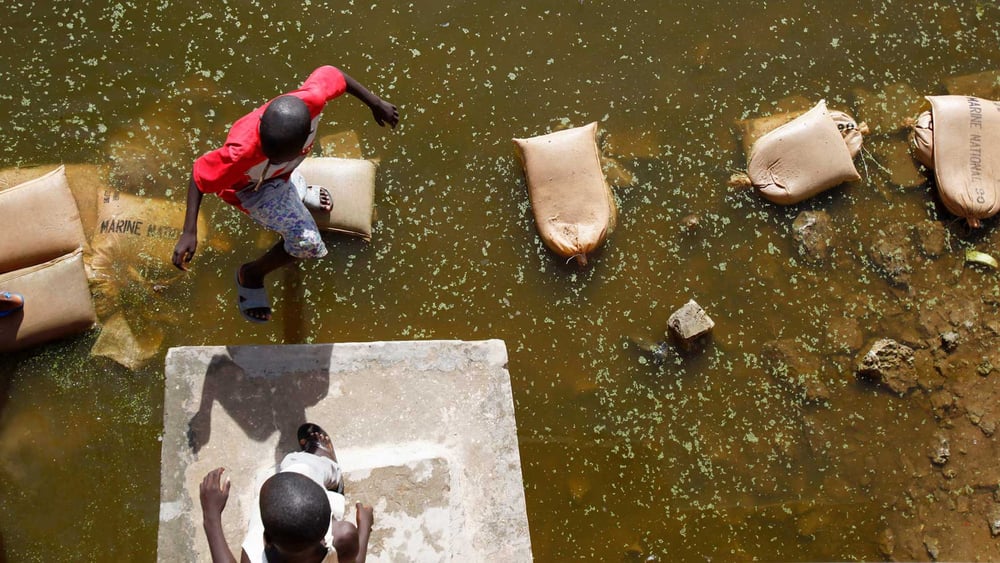 Ein Laufsteg aus Sandsäcken: Nach starken Regenfällen in einem Vorort von Dakar behilft sich die Bevölkerung mit Notlösungen. © Keystone/AP/Rebecca Blackwell