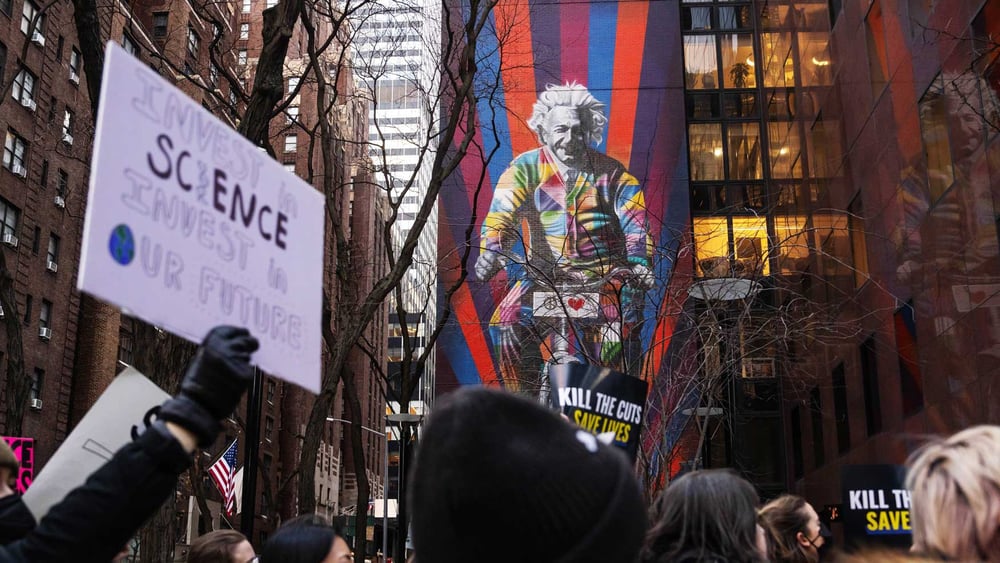 Vor dem Einstein-Wandbild in New York protestieren Demonstrant*innen gegen die beschlossenen Kürzungen bei der medizinischen Forschung und Gesundheitsversorgung.  © Adam Gray / Bloomberg via Getty Images