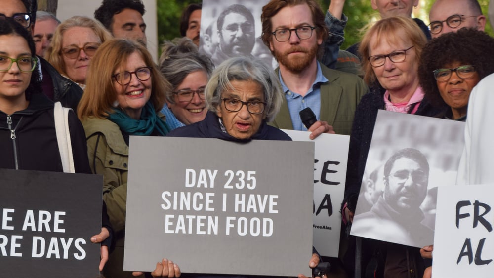 Laila Soueif umgeben von Mitstreiter*innen mit einem Transparent, auf welchem steht: Day 235 since I have eaten food.