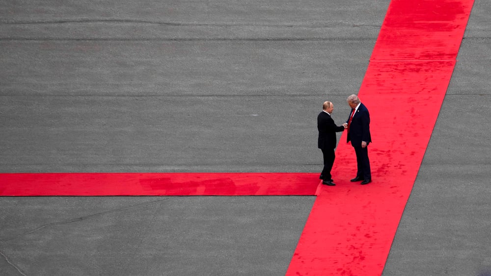 Präsident Putin und Präsident Trump schütteln sich auf einem langen roten Teppich die Hände.