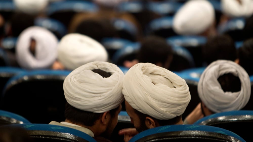 Sitzende Männer mit weissen Turbanen, von hinten gesehen. Zwei tuscheln miteinander.