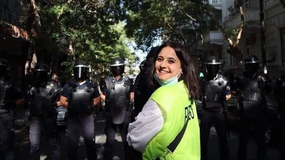 Bild von Nargiz Absalamova mit einer Leuchtweste, im Hintergrund eine Gruppe von Polizisten, die wahrscheinlich die Kundgebung eindämmen
