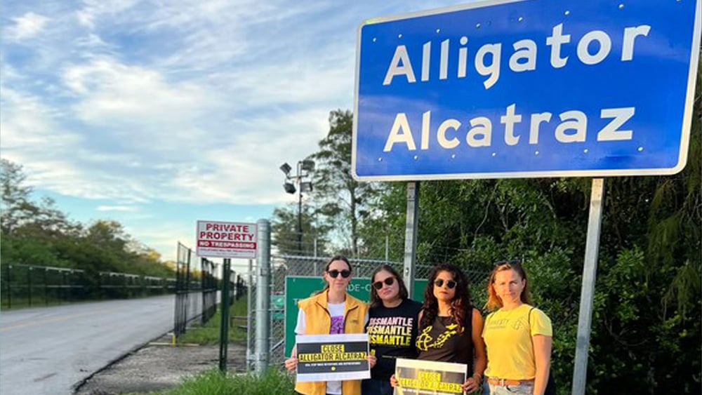 Amnesty Aktivist*innen vor dem Ortschild «Alligator Alcatraz»