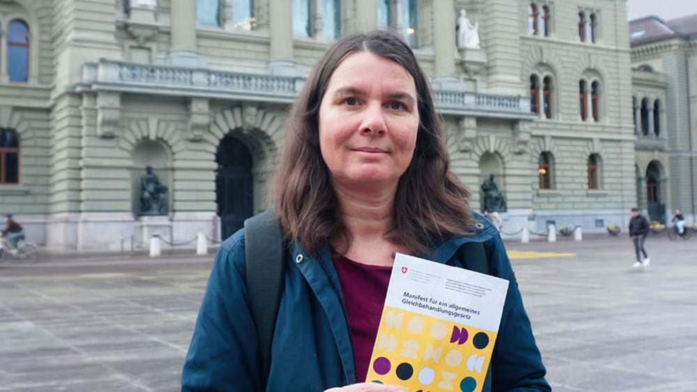 Die junge Frau steht auf dem Bundesplatz vor dem Bundeshaus mit dem Manifest in der Hand.