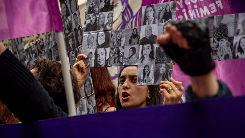 Frauen mit Fahnen und Transparenten mit Bildern wohl getöteter Frauen demonstrieren mit erhobenen Armen.