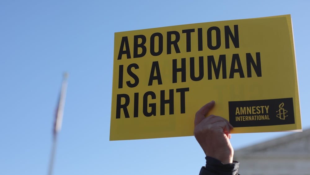 Eine Hand hält ein gelbes Amnesty-Transparent mit der Aufschrift «Abortion is a Human Right»