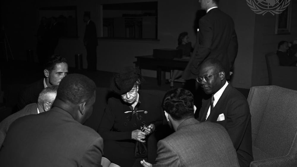 Schwarzweiss-Bild von Eleanor Roosevelt, Vorsitzende der Menschenrechtskommission, die mit fünf Vertretern der haitianischen Delegation sitzend diskutiert.