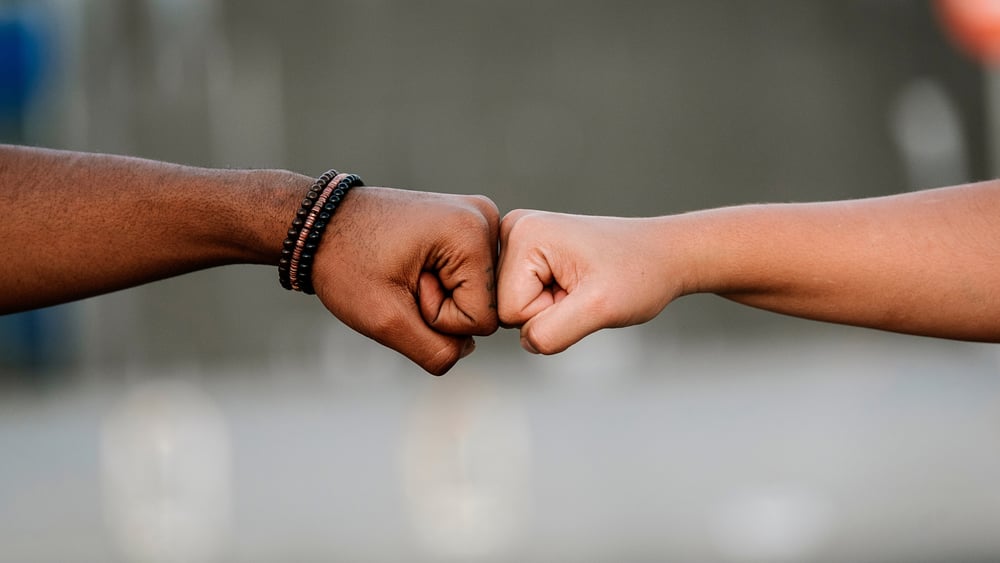 Symbolbild mit einer weissen und einer schwarzen Faust, die sich berühren.