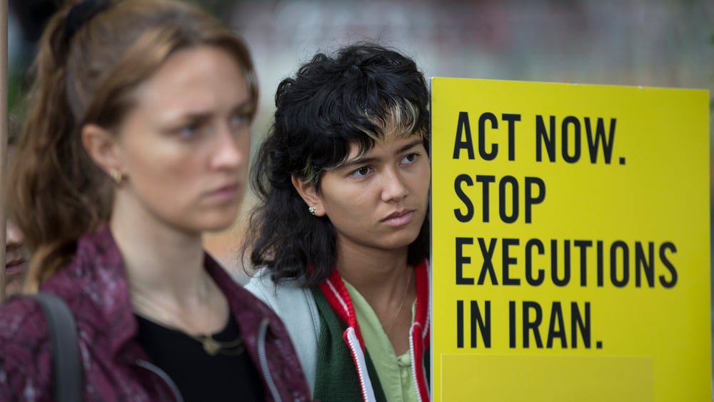 Zwei Demonstrantinnen halten ein Plakat hoch, auf dem steht "Act Now - stop executions in Iran"