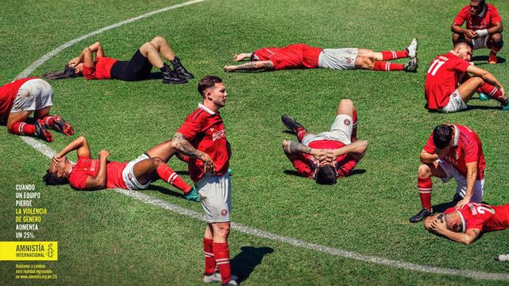 Des joueurs sont allongés sur le terrain, sur le ventre ou sur le dos, tête dans les mains. Un arbitre regarde au loin.