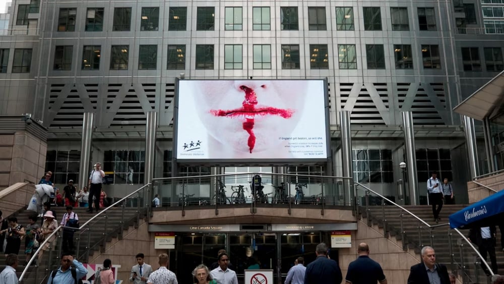Dans le hall d'un grand bâtiment, une affiche montre le visage d'une femme ensanglanté.
