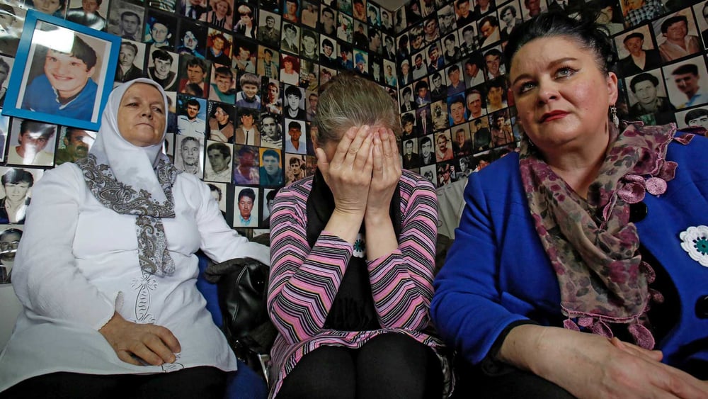 Entourées de photos de personnes disparues, des femmes bosniennes sont rassemblées à Tuzla (Bosnie), dans les locaux de l’Union des mères de Srebrenica, pour regarder la retransmission du procès de Radovan Karadzic par le Tribunal pénal international pour l’ex-Yougoslavie en 2016. © AP Photo/Amel Emric