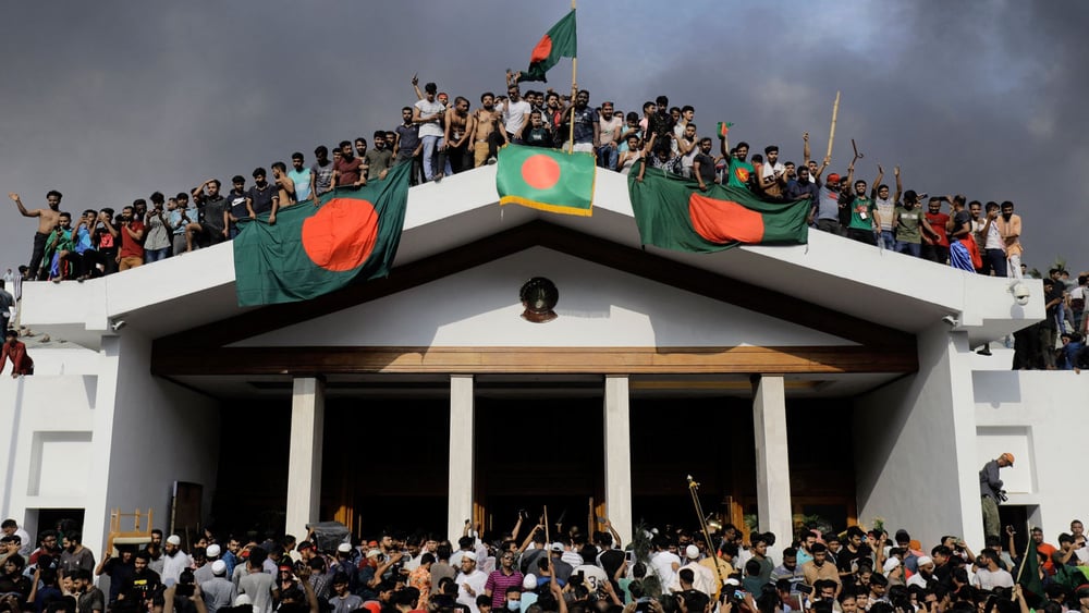 Des manifestant·e·x·s anti-gouvernementaux avec le drapeau national bangladais alors qu'ils prennent d'assaut le palais du Premier ministre Sheikh Hasina à Dhaka le 5 août 2024 © K M ASAD/AFP via Getty Images