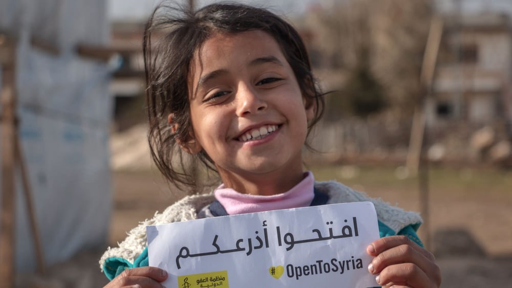 Un enfant syrien dans un camp à Bekaa Tal au Liban, avec un panneau de la campagne d'Amnesty de soutien aux réfugié·e·s syriens. © Amnesty International