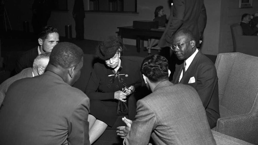 Photo en noir et blanc d'Eleanor Roosevelt, présidente de la Commission des droits de l'homme, en train de discuter, assise, avec cinq représentants de la délégation haïtienne.