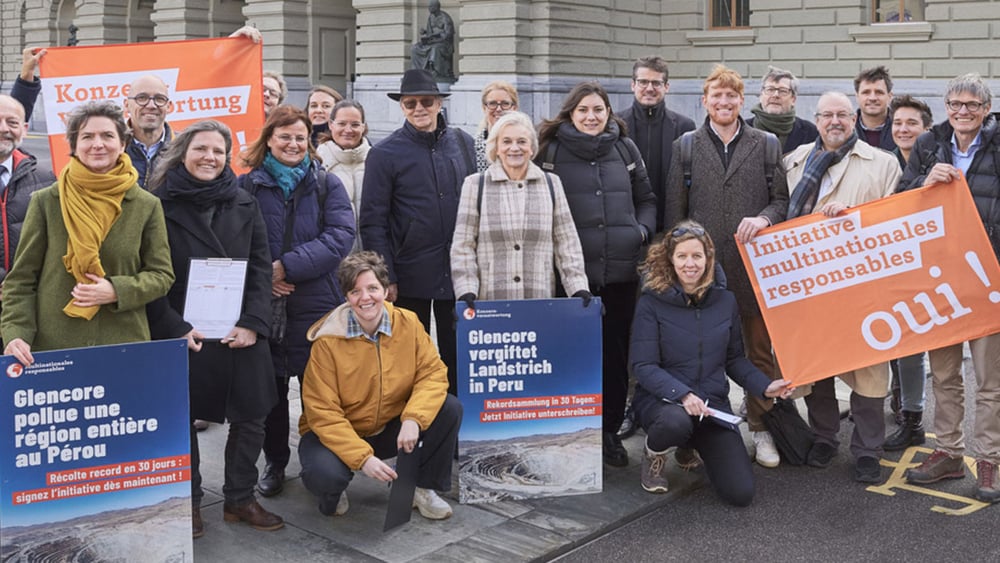 Des activistes brandissant des drapeaux de l'initiative ainsi que des pancartes sur lesquelles on peut lire : « Glencore empoisonne une région du Pérou » devant le Palais fédéral, à Berne.