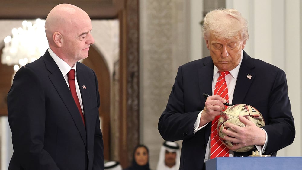 Gianni Infantino insiema a Donal Trump, che sta firmando un pallone di calcio.