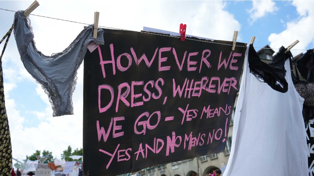 Una corda da bucato con uno slip e una canottiera; in mezzo è appeso un foglio su cui c'è scritto: "However we dress, whereever we go - Yes means Yes and No means No" (In qualsiasi modo ci vestiamo, ovunque andiamo – Sì significa sì e no significa no).