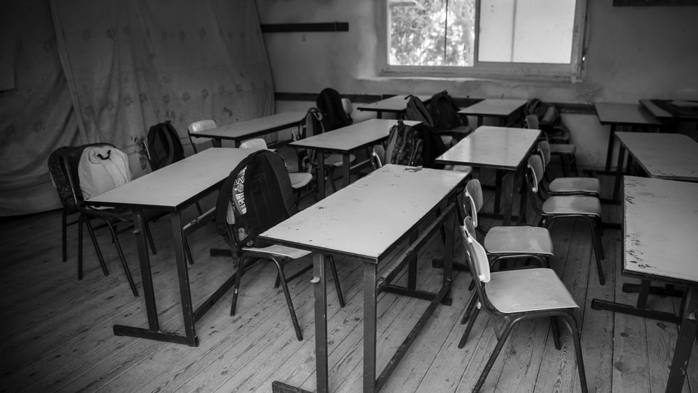 Aula scolastica con sedie e tavoli semplici.