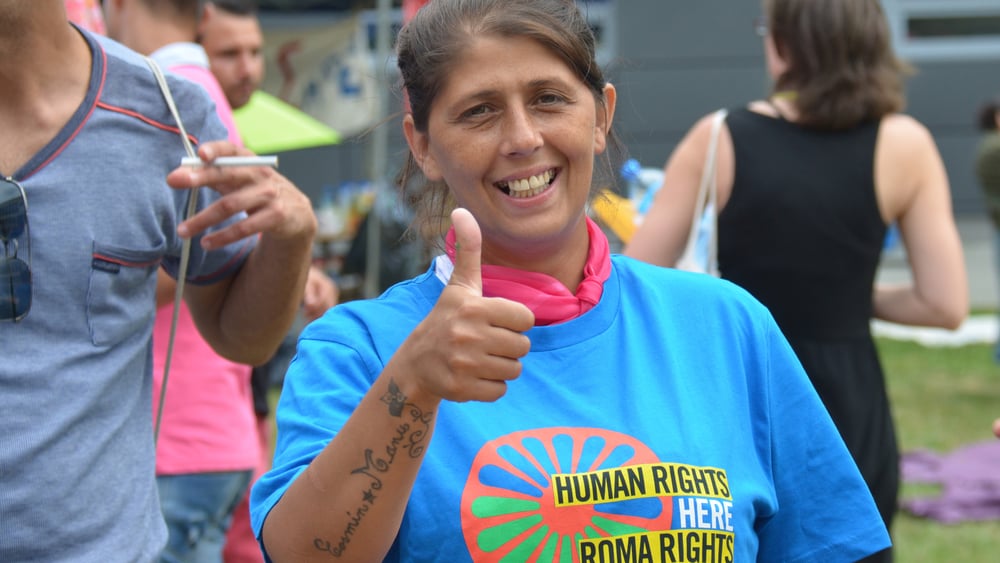 Una donna con una maglietta con la scritta: «Human Rights - Roma Rights» alza il pollice in segno di «OK».
