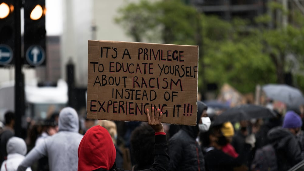 Striscione di una manifestazione Black Lives Matter con una scritta in inglese che dice “È un privilegio poter imparare qualcosa sul razzismo invece di subirlo”.