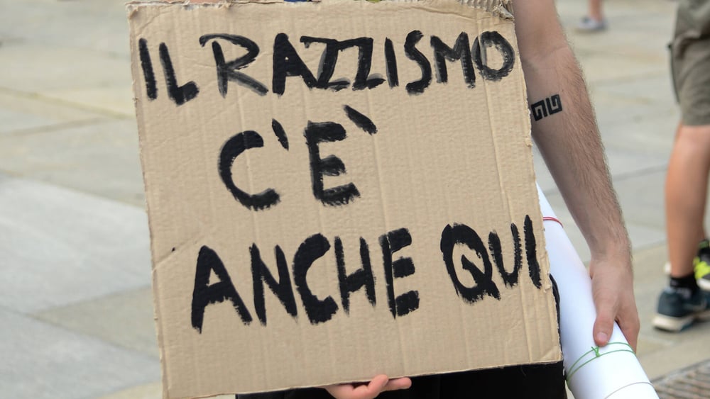 Un cartello con lo slogan "Il razzismo c'è anche qui"