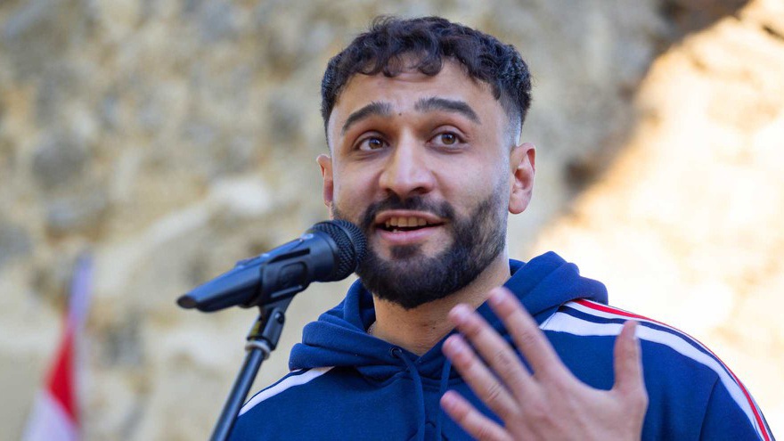 Porträt von Géza Buzás Habel: Er spricht in ein Microfon und gestikuliert dabei mit der linken Hand