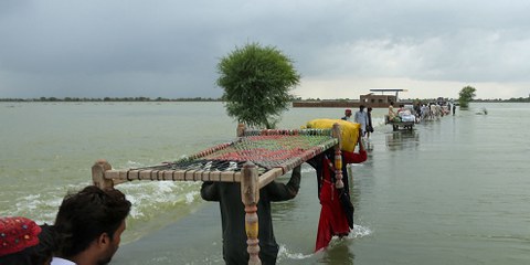 Menschen verlassen ihre Dörfer und tragen ihre Habseligkeiten durch überschwemmte Ebenen, um in höher gelegene Gebiete im südlichen Punjab zu erreichen, 25. August 2022. © Getty / Shahid Saeed Mirza