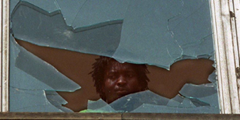 23. September 1991: Nach Angriffen auf eine Flüchtlingsunterkunft im sächsichen Hoyerswerda schaut ein Bewohner aus einem zerstörten Fenster: © Zentralbild / pa