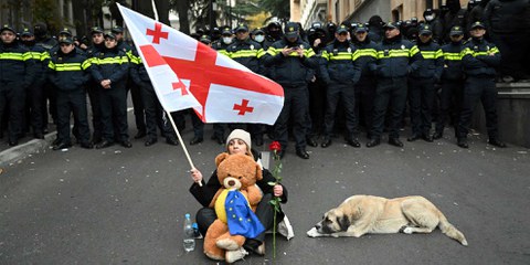 Eine Frau hält eine rote Rose und eine georgische Flagge in der Hand, während sie bei einem Protest gegen die Ergebnisse der Parlamentswahlen des Vormonats am 25. November 2024 in Tiflis Polizisten gegenübersteht, als das Parlament zu seiner ersten Sitzung zusammentritt. © AFP via Getty Images