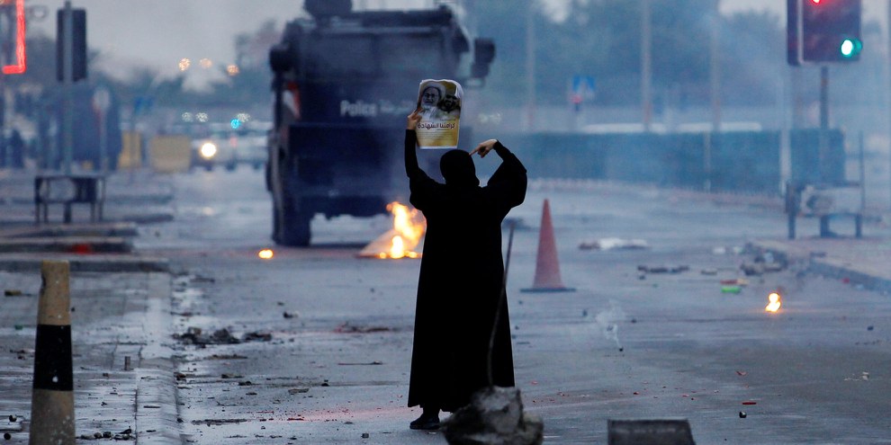 Eine Demonstrantin mit einem Bild eines schiitischen Geistlichen stellt sich vor bewaffnete Polizeiwagen.© REUTERS/Hamad I Mohammed