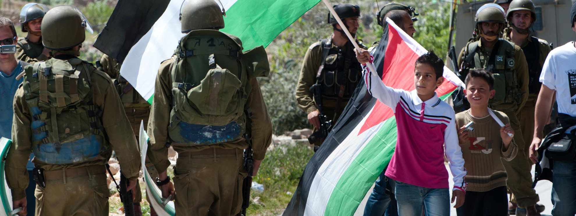 Ein palästinensischer Junge schwingt die palästinensische Fahne vor dem Gesicht eines israelischen Soldaten anlässlich eines Protestmarschs gegen die Trennmauer in Al-Masara. © Ryan Rodrick Beiler / Shutterstock.com