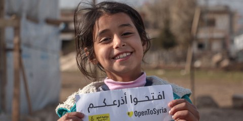 Ein syrisches Kind in einem Lager im Bekaa Tal im Libanon mit einem Schild der Amnesty Kampagne «Open Your Eyes - Open Your Arms - Open your hearts» zur Unterstützung der Geflüchteten. © Amnesty International