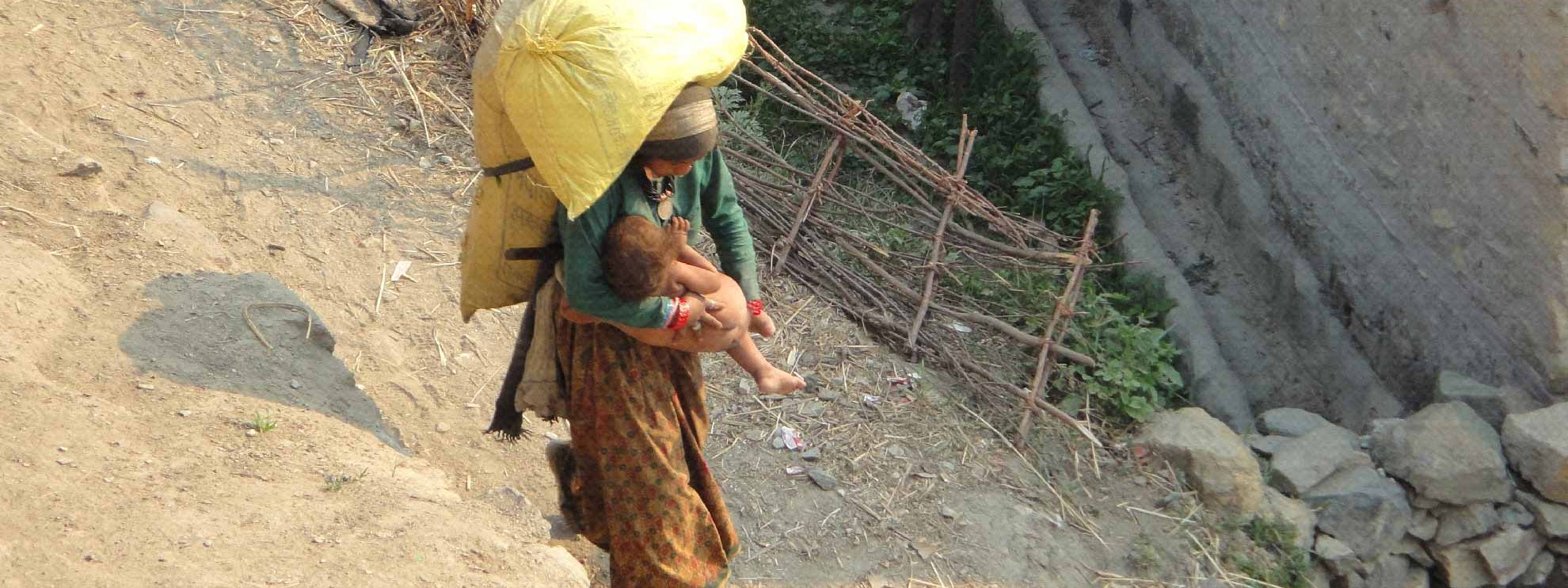Eine Frau trägt schwere Lasten und ein Kind im Mugu District, Nepal 2013 © Amnesty International