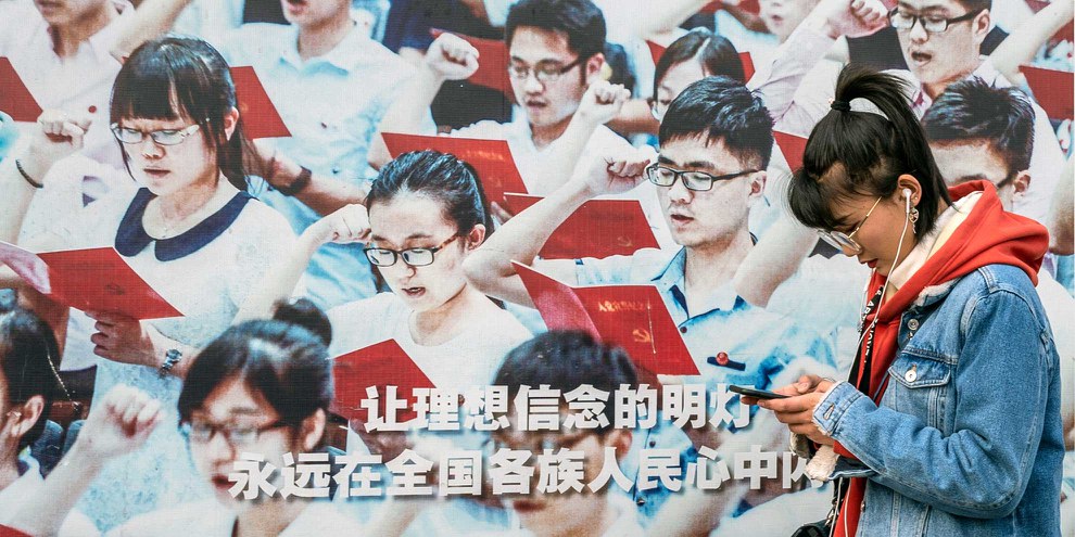 Zwischen moderner Medienwelt und klassischer Propaganda: Eine junge Chinesin vor einem Werbeplakat im Vorfeld des Volkskongresses 2019. © KEYSTONE/EP/Roman Pilipey