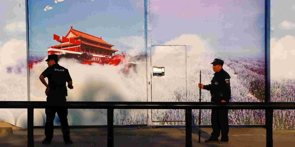 Sicherheitskräfte vor einer Einrichtung, die offiziell als «Berufsbildungszentrum» gilt, im Bezirk Huocheng in Xinjiang. Die hohen Zäune des Zentrums sind mit Propaganda-Bannern versehen, das Eingangstor mit grossen Fotopostern. © REUTERS/Thomas Peter
