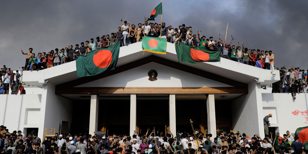 Des manifestant·e·x·s anti-gouvernementaux avec le drapeau national bangladais alors qu'ils prennent d'assaut le palais du Premier ministre Sheikh Hasina à Dhaka le 5 août 2024 © K M ASAD/AFP via Getty Images