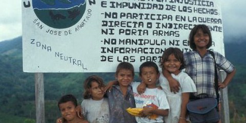 Des enfants de la communauté San José de Apartado posent devant un panneau qui annonce la zone neutre. © DR