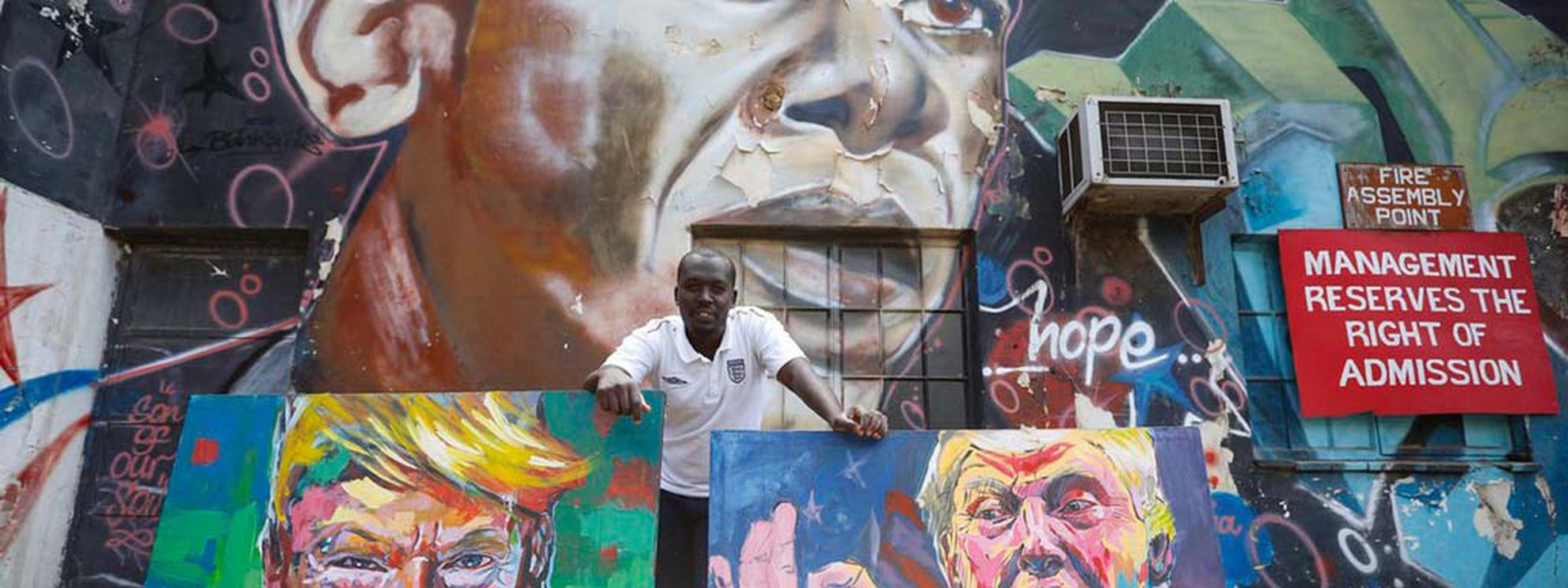 L’artiste kenyan Yegonizer et ses portraits de Donald Trump, devant une oeuvre murale de Bankslave représentant Obama. © Keystone/EPA/DAI KUROKAWA