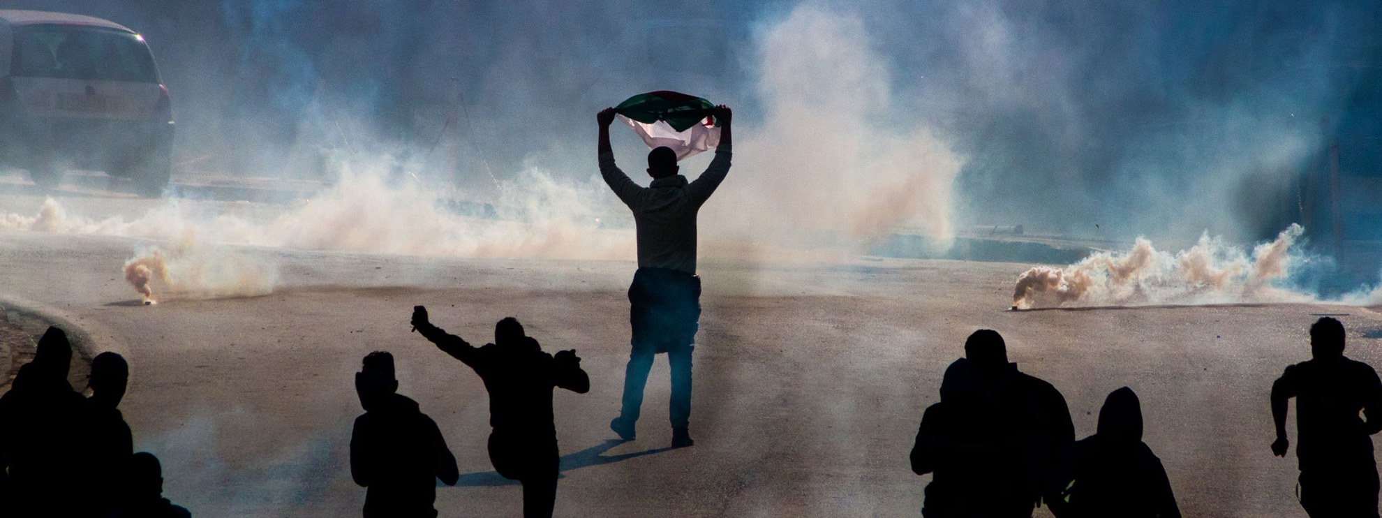 Tenant un drapeau algérien, un manifestant affronte la police lors d'une manifestation contre le président, le 29 mars 2019. @ BkhStudio