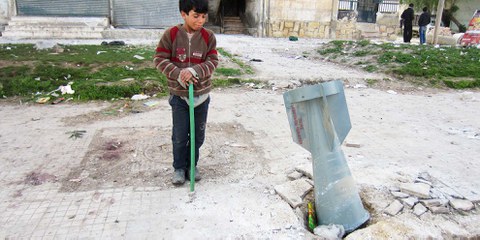 Un enfant regarde une bombe à sous-munitions larguée à Alep, en 2013. Des armes de ce type sont utilisées également dans des bombardements touchant la population civile en Ghouta orientale. © Amnesty International