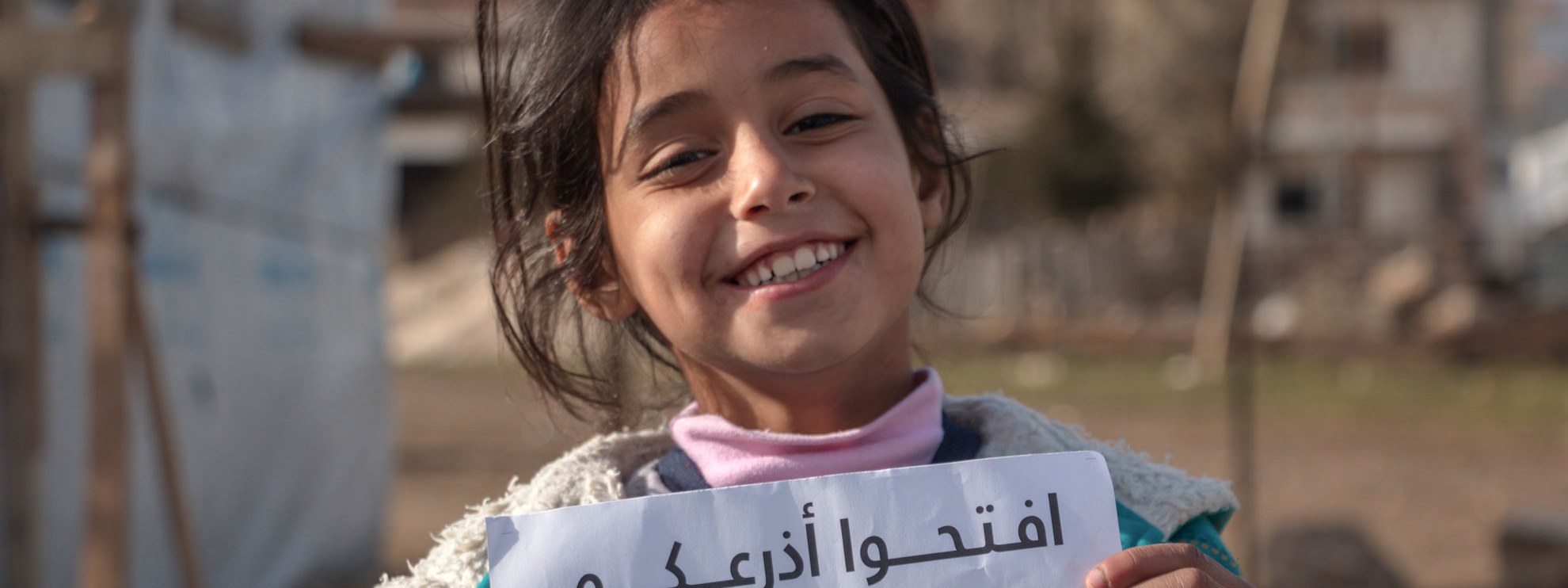 Un enfant syrien dans un camp à Bekaa Tal au Liban, avec un panneau de la campagne d'Amnesty de soutien aux réfugié·e·s syriens. © Amnesty International